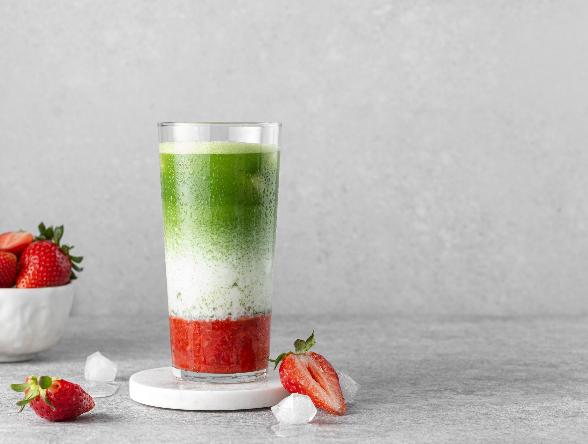 Strawberry matcha latte served in high ball glass with ice cubes, fresh berries, strawberry puree and matcha green tea.