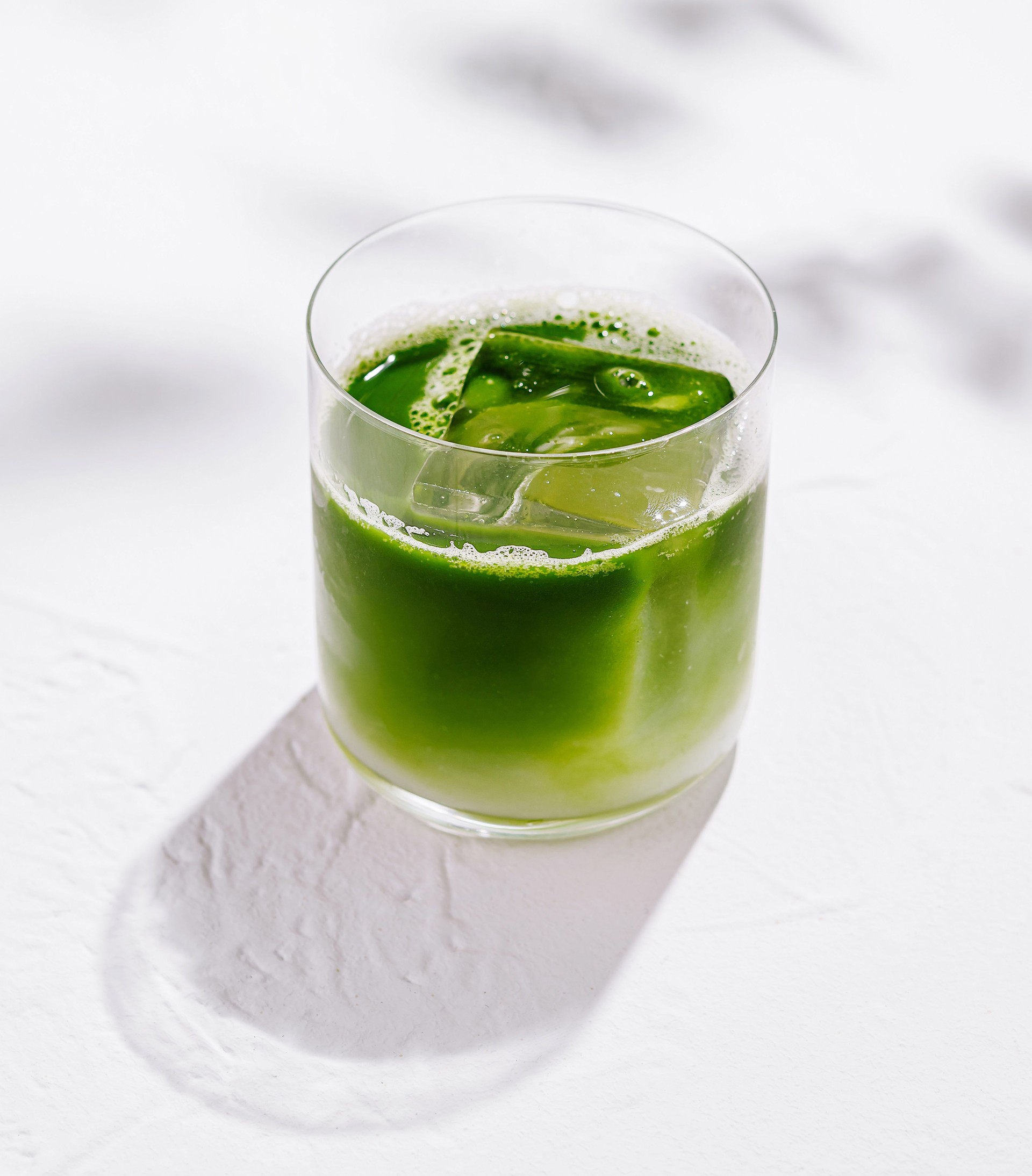 Green iced matcha latte standing on white table with leaf shadows